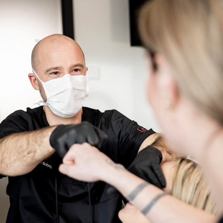 Ein Zahnarzt mit Mundschutz begrüßt eine Patientin